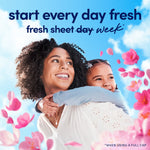 Smiling woman carrying a child surrounded by pink flower petals with text promoting freshness for Downy.