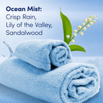 Rolled blue towels with a lily-of-the-valley sprig and text describing Ocean Mist scent notes.
