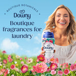 Smiling woman holding a Downy Peonia scent booster bottle amid a field of pink flowers