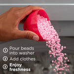 Hand pouring pink Downy scent booster beads from a red measuring cup into a washing machine drum with instructions text
