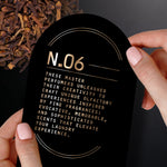 Hands holding a black card labeled N.06 with descriptive copy, shown against a background of whole cloves.
