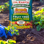 Dr. Earth Natural Wonder Fruit Tree Fertilizer bag placed in a garden bed near strawberry plants and gardening gloves