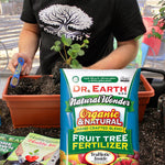 Lifestyle photo of a person potting a plant with a Dr. Earth Natural Wonder Fruit Tree Fertilizer bag visible in foreground