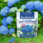 Product lifestyle image of a Dr. Earth Pelletized Soil Acidifier pouch placed in front of blooming blue hydrangeas in a garden.