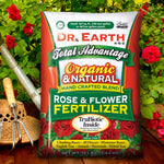 Dr. Earth Total Advantage Rose & Flower fertilizer bag staged outdoors among rose bushes with gardening tools visible to the left
