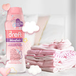 Dreft Blissfuls bottle shown on a soft-focused background next to a stack of folded baby clothes and decorative cloud and heart graphics.
