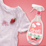 Dreft bottle next to a stained white shirt with a strawberry and stain demo on a pink background