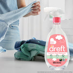 Dreft spray bottle staged on a countertop with folded baby clothes and a person handling a garment