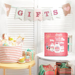 Styled gift scene with a Dreft Bundle of Bliss pink gift box on a small table under a 'GIFTS' banner and decorated basket.