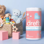 Dreft wipes tub next to a basket of children's toys on a pastel blue background, product label clearly visible