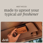 Hand attaching a Drift wooden car freshener to a vehicle visor, showing the wood grain and logo inside a car.