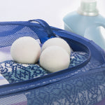 Three wool dryer balls inside a blue mesh laundry bag with detergent bottle in background