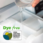 Close-up of liquid being poured into a washer dispenser tray with 'Dye free' text and USDA Certified Biobased Product badge