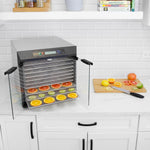Kitchen countertop scene with an electric food dehydrator showing multiple mesh trays and sliced citrus on lower racks.