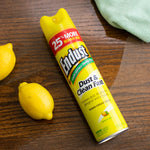 Angled product shot of an Endust lemon zest aerosol can on a wood surface with lemons and a cloth nearby