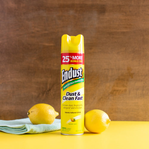 Centered Endust lemon zest aerosol can standing on a yellow surface with lemons and a cloth against a wood backdrop