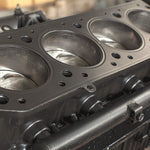 Close-up of a metal engine cylinder block showing piston bores and gasket surface with detailed machining texture.