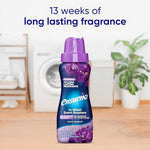 Ensueño Violet Bouquet in-wash scent booster bottle staged on a wooden floor with washing machine and plants in background