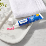 Tube of Equate denture adhesive cream with pink adhesive squeezed onto a tray beside a white towel