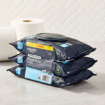 Three navy Equate flushable wipes packs stacked on a counter with a plastic flip-top lid and blurred toilet paper in background