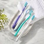Four Equate manual toothbrushes arranged on a tray with a white towel and decorative plant on a marble surface