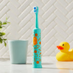 Blue-green Equate kids electric toothbrush standing on a bathroom counter with a cup and rubber duck prop in soft-focus background.