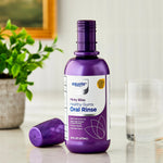 Purple Equate oral rinse bottle with cap removed, shown on a bathroom countertop with a glass and plant.