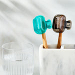 Two clip-on toothbrush protectors clipped onto toothbrush heads placed in a marble holder next to a glass