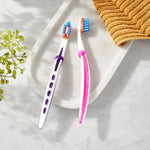 Styled lifestyle shot of two Equate toothbrushes on a white tray next to a folded towel and greenery.
