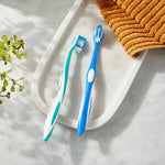 Two Equate manual toothbrushes, one blue and one teal, displayed on a bathroom tray with a folded orange towel nearby.