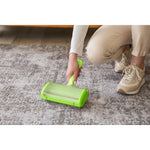 Person using a green Evercare pet hair remover on a patterned gray area rug, showing product in use