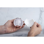 Pair of hands holding the clear gel lint ball and its white protective casing on a marble surface
