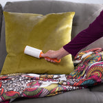 Hand using an Evercare lint roller with orange handle on a green velvet cushion on a couch