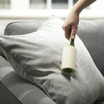 Hand using an Evercare green-handled lint roller on a grey fabric sofa cushion to remove lint