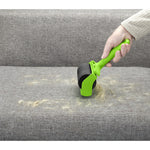 Hand using green Evercare lint roller on grey upholstered sofa removing pet hair