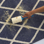 Hand using an Evercare lint roller to pick up crumbs from a navy and white patterned rug.