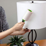 Person using an Evercare lint roller with green handle to clean a white lamp shade in a living room scene