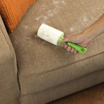 Hand using Evercare green-handled lint roller on a beige fabric sofa with visible pet hair