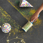 Hand rolling an Evercare lint roller over a dark surface covered in colorful confetti and party hat pieces