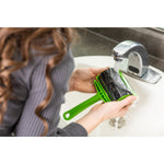Hands rinsing a black gel roller insert from a green Evercare lint roller under a sink faucet