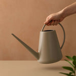 Hand holding a birch grey Expert Gardener resin watering can over a neutral backdrop