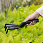 Hand holding Expert Gardener poly cultivator over a blurred background of green foliage, showing tool angle and grip.