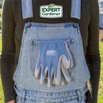 Expert Gardener gloves tucked into the front pocket of denim overalls with brand logo above