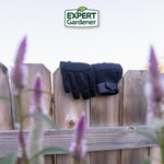 Pair of black Expert Gardener gloves draped over a wooden fence with blurred flowers in the foreground and logo above