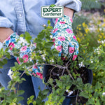Close-up lifestyle photo of hands in Expert Gardener floral gloves tending a potted plant, with brand logo above
