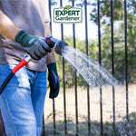 Person wearing Expert Gardener gloves holding a garden hose nozzle spraying water next to a fence