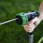 Hand-held garden spray nozzle with green head emitting a focused jet of water outdoors