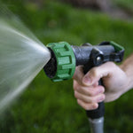 Hand holding a green-tipped garden nozzle spraying a wide fan of water over grass