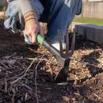 Close gardening scene of hand hoe cultivator digging in soil with a person’s hand holding the green handle