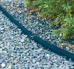Metal landscape pin securing a black landscape edging strip against gravel and adjacent shrubbery.